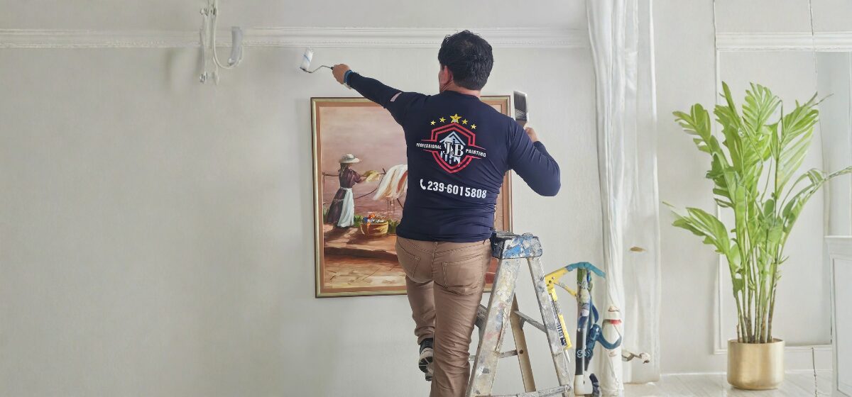 Person painting wall near framed artwork.